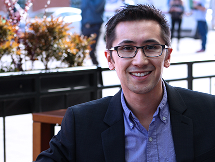 Paul Nguyen Headshot. Asian male sitting down outside on a chair posing for the camera.